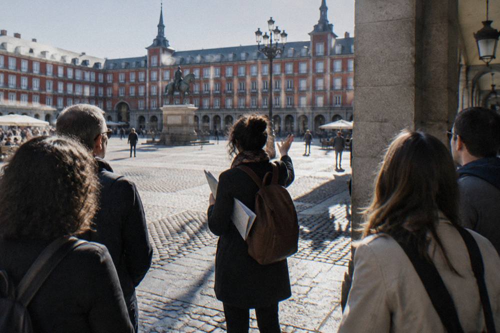 A guide with a small group standing in a sunlit old Madrid square