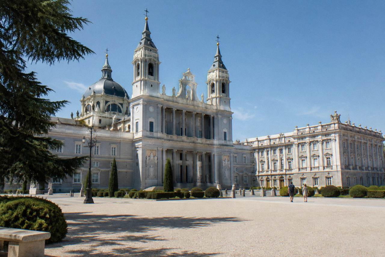 The neoclassical facade of Almudena Cathedral beside the Royal Palace under a clear sky