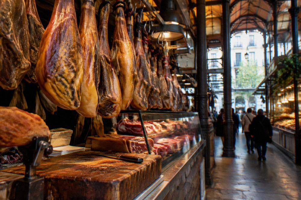 Market stall counter with cured hams hanging above a glass display case