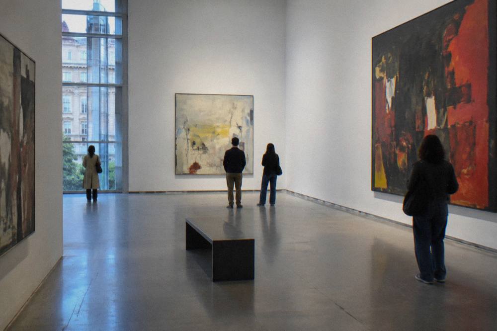 Gallery interior of the Reina Sofia Museum with visitors viewing large modern paintings under bright lighting