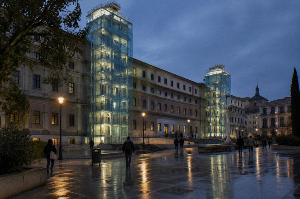 Exterior view of the Reina Sofia Museum at dusk with the glass elevator towers illuminated