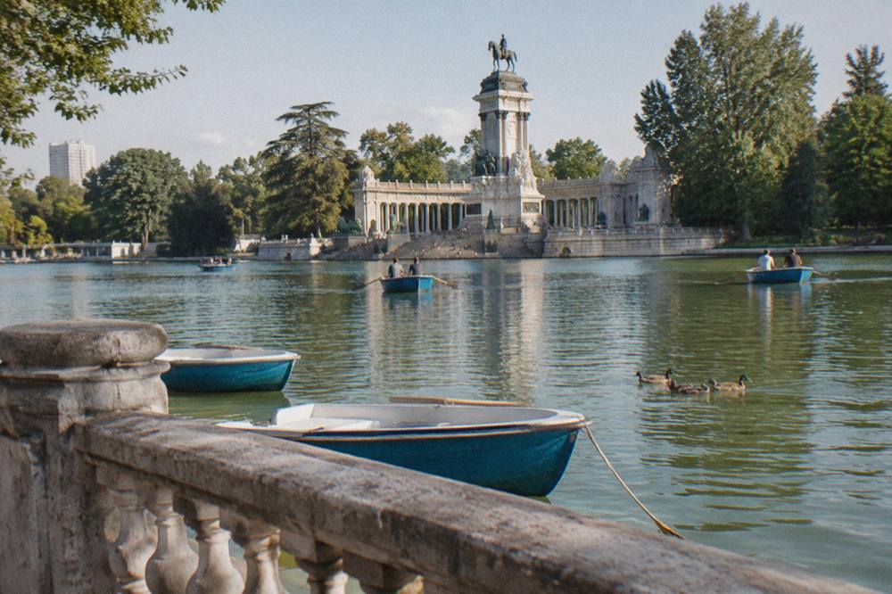 Rowboats floating on the lake in Retiro Park with stone balustrades and trees behind them