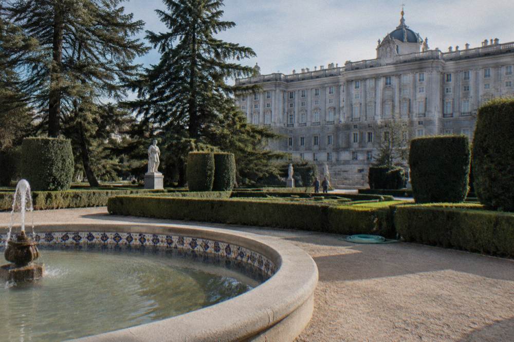 Formal garden with trimmed hedges, fountains and a large palace facade in the background