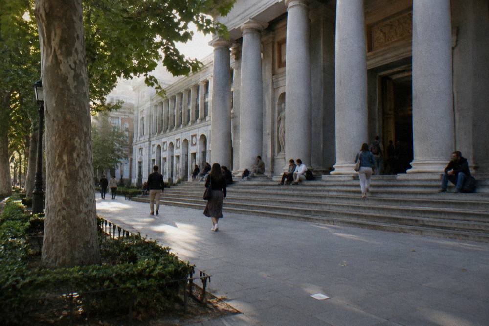 Exterior facade of the Prado Museum with stone columns and visitors gathered on the steps
