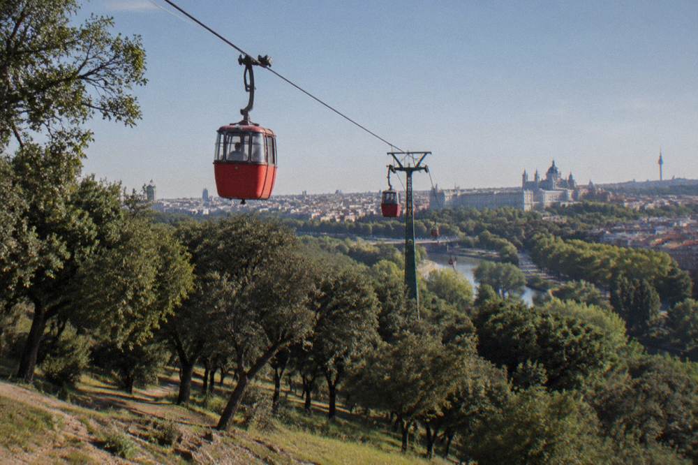 Cable car cabins travelling above trees toward a city skyline