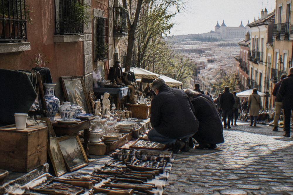 Crowded flea market stalls with antiques and second-hand goods on a sloped Madrid street