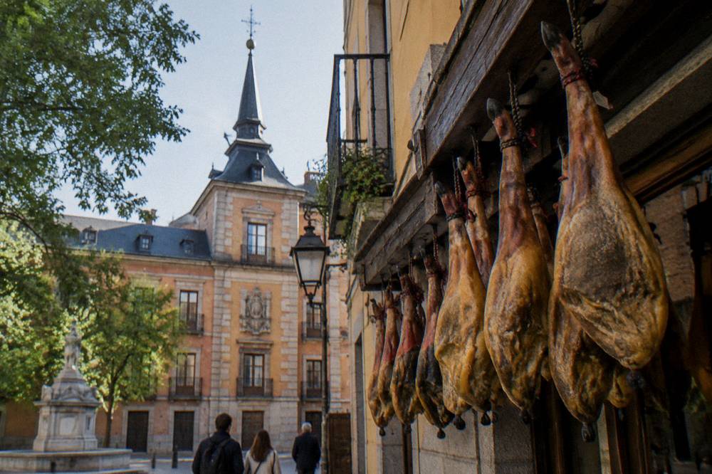 Standing customers at a traditional Madrid tavern counter with hanging ham