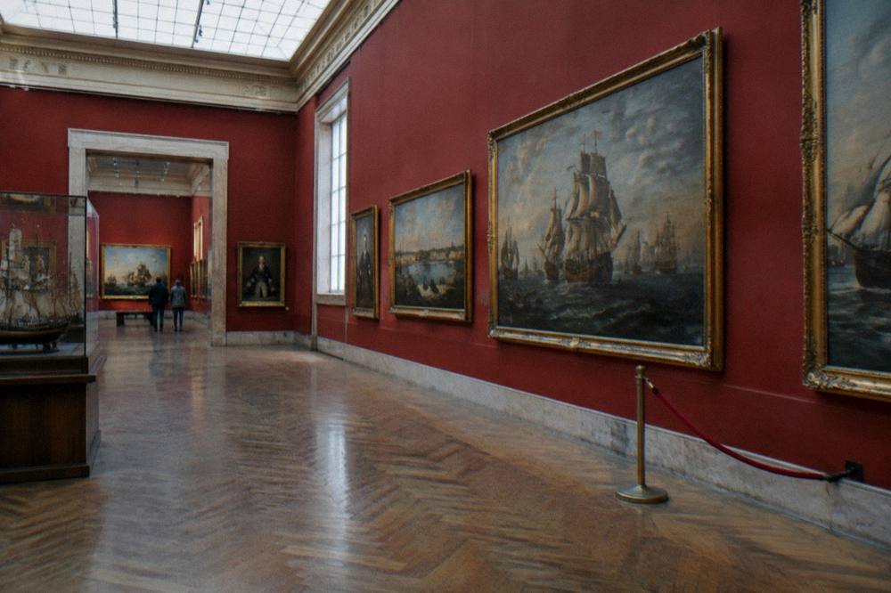 Classical museum gallery with paintings on deep red walls and skylight from above