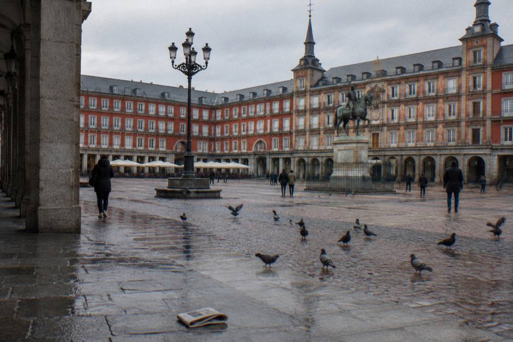 Plaza Mayor in Madrid with red facades and statue under an overcast sky