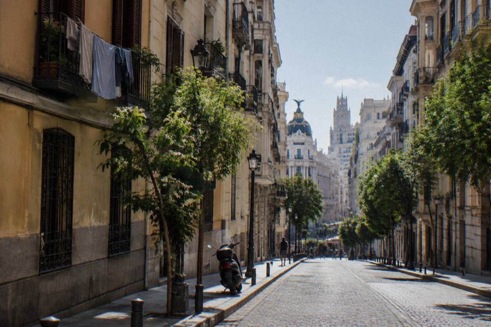 A narrow central Madrid street with tall shuttered buildings and sunlight on the cobblestones
