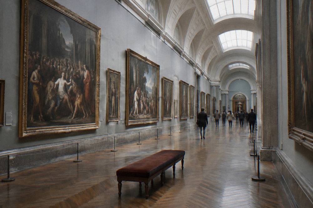 A gallery hall with classical paintings hung in rows under soft ceiling light