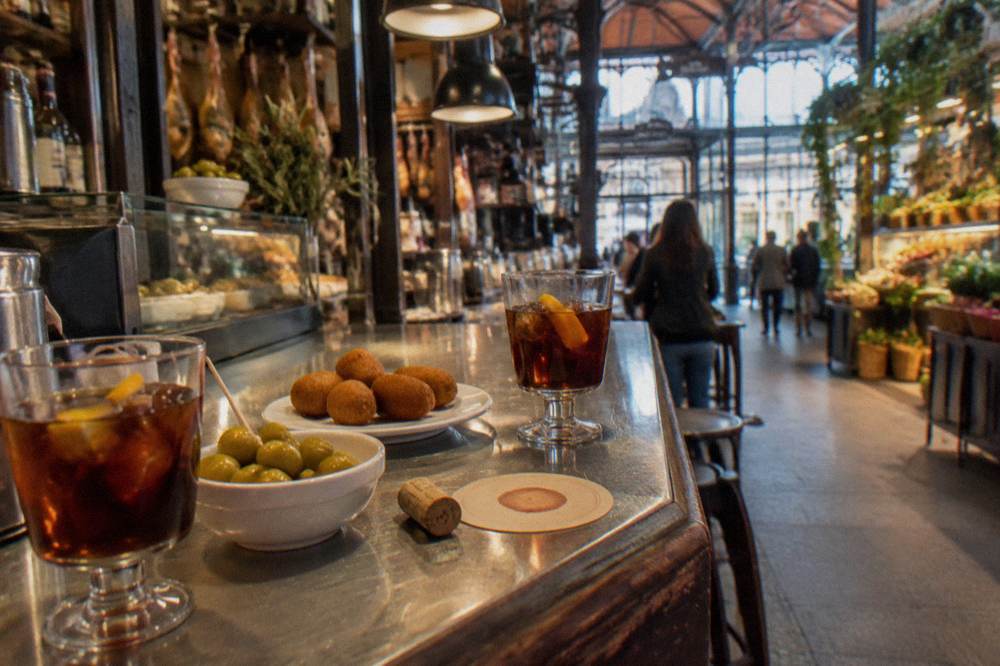 A tapas bar counter with small plates and glasses of vermouth on a wooden bar top