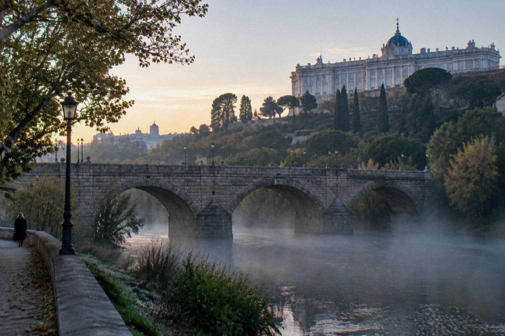 Stone bridge arches over the Manzanares with palace gardens on the high ground above