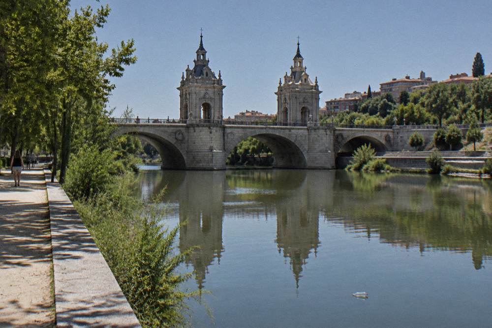 Baroque stone bridge with twin towers reflected in the Manzanares river at midday