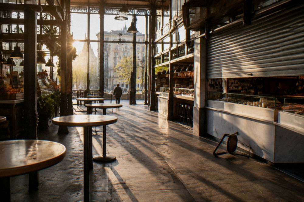 Sunlight entering a glass market hall over empty standing tables