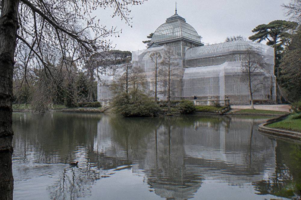 Ornate glass and iron pavilion reflected in a pond surrounded by trees in a large public park